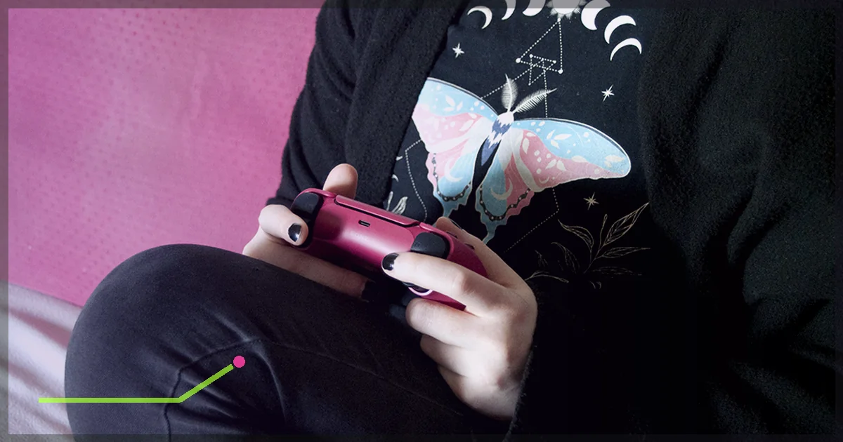 Player holding a game controller while seated against a pink background