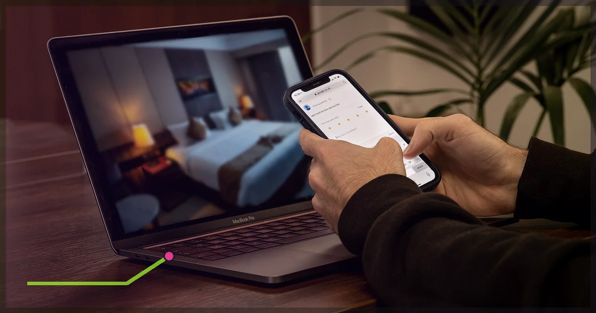 Traveler using a phone beside a laptop displaying a hotel room